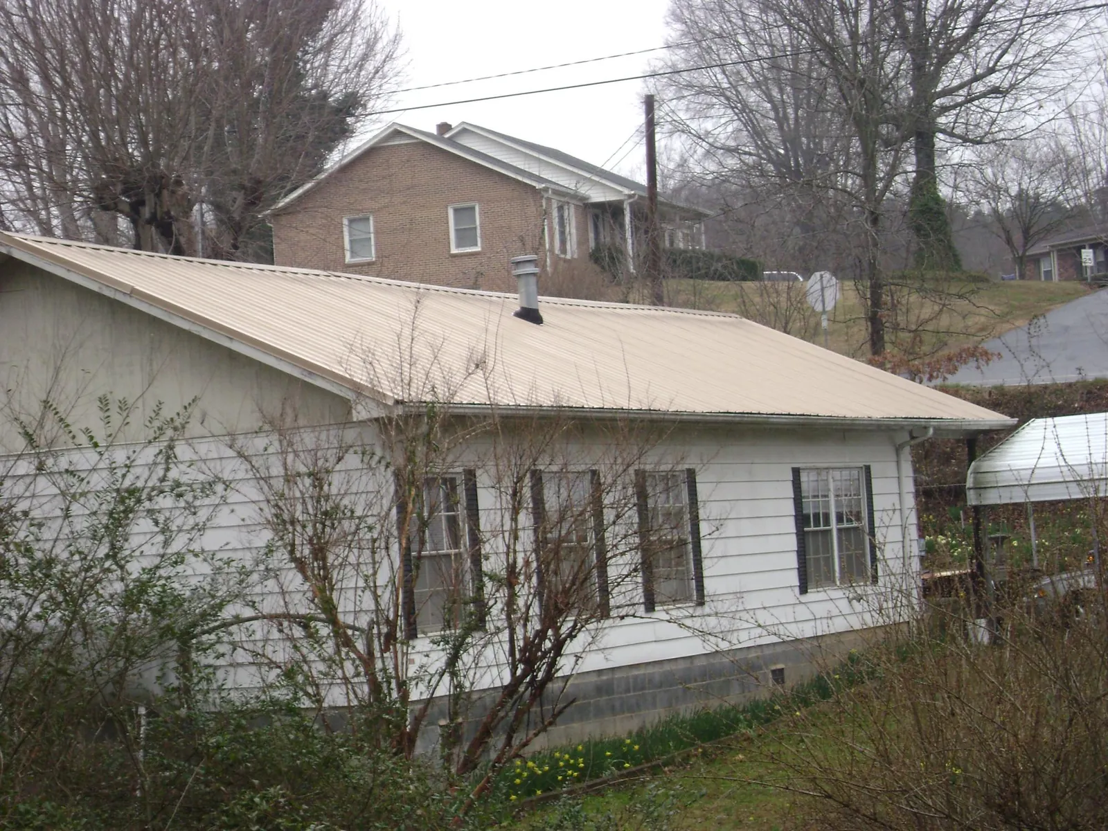 Tan metal roof on a white sided house set into a hillside — Commercial Roofing by Roofing Brothers in Gladstone